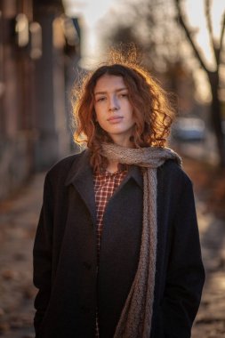 Olağanüstü kıvırcık kızıl saçlı genç bir kadın şehir merkezindeki sokakta kameraya bakıyor. Kadın portresi.