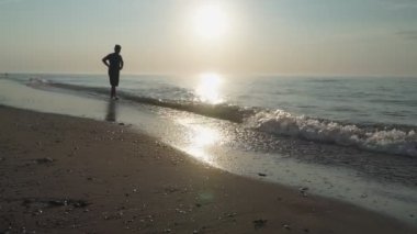Gün doğumunda ıssız bir sahilde huzur içinde yürüyen bir adam silueti. deniz manzarası