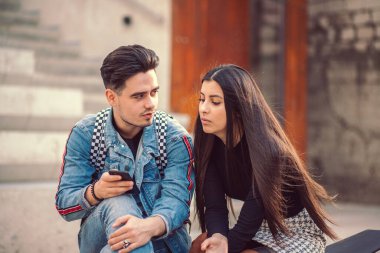 Genç bir çiftin portresi parkta bir bankta oturur ve akıllı telefondaki fotoğraflara bakar.