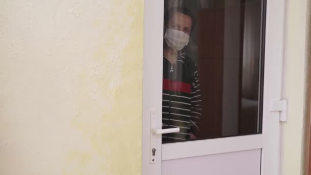 Uma mulher com uma máscara médica abre a porta e sai de casa. Covid-19 . — Vídeo de Stock