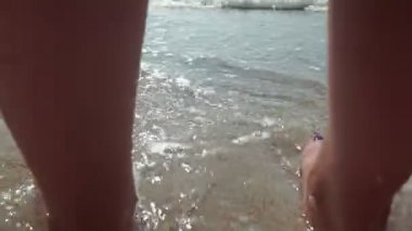 Yanık tenli kadın ayakları üzerinde yıkama dalgalar deniz. Güzel ve genç birbayan rahatlatıcı yaz tatili sırasında kıyısında. Güneşli bir günde sahilde yatan kız bacaklar. Yavaş hareket kapatmak