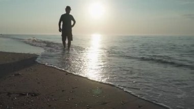 Gün doğumunda ıssız bir sahilde huzur içinde yürüyen bir adam silueti. deniz manzarası
