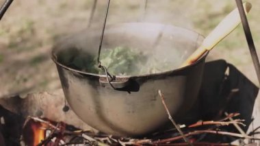 Yemek bir kazanda hazırlanır. Bovlingci kazıkta kaynıyor, arka planda ise bir çiçek tarlası var..