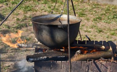 Yemek bir kazanda hazırlanır. Bovlingci kazıkta kaynıyor, arka planda ise bir çiçek tarlası var..