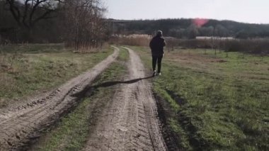 Genç bir kadın köy yolunda yürüyor ve telefonla konuşuyor.