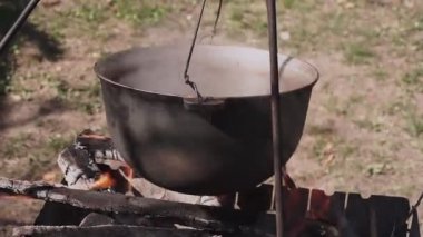 Yemek bir kazanda hazırlanır. Bovlingci kazıkta kaynıyor, arka planda ise bir çiçek tarlası var..