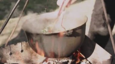 Yemek bir kazanda hazırlanır. Bovlingci kazıkta kaynıyor, arka planda ise bir çiçek tarlası var..