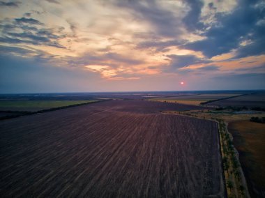 Sıcak bir yaz günbatımı tonu ile kırsal alan üzerindeki hava manzarası. Tarım arazisi orman ve çayırlarla karışıyor. Eğri nehir boyunca yeşil ekin tarlaları. Ağaçlar uzun gölgeler oluşturuyor.