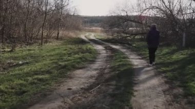 Genç bir kadın köy yolunda yürüyor ve telefonla konuşuyor.