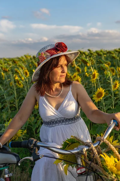 Žena Klobouku Bílých Šatech Bicyklem Prochází Pylem Slunečnicemi — Stock fotografie