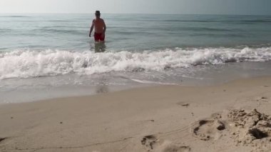 Yetişkin bir adam deniz suyundan deniz manzarasının arka planında çıkar.