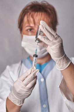 Doktor aşıyı şırıngaya koyar. Cam şişe bir teknisyenin elinde. Tedavisi olan bir şişe silikon eldivenlerde el tutar. Tedavide bir atılım. Aşı muayeneleri. Salgın.