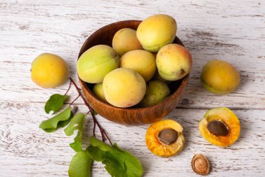 Olgun organik kayısılar, beyaz ahşap bir arka planda, dişbudak ağacı ahşap kasede meyveler.