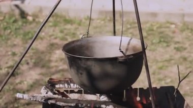 Yemek bir kazanda hazırlanır. Bovlingci kazıkta kaynıyor, arka planda ise bir çiçek tarlası var..