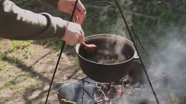 М'ясо з рисом і овочами готують в котлі на вогнищі. Кухар перемішує інгредієнти з віночком. Приготування пілафу . — стокове відео