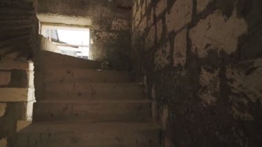 Bir adam yarım kalmış, birinci şahıs manzaralı, çok katlı, terk edilmemiş bir evin merdivenlerine tırmanır.