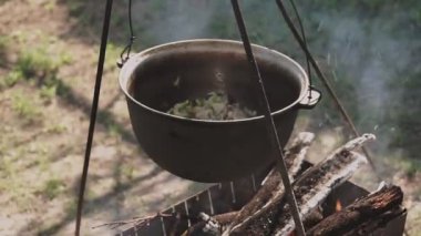 Yemek bir kazanda hazırlanır. Bovlingci kazıkta kaynıyor, arka planda ise bir çiçek tarlası var..