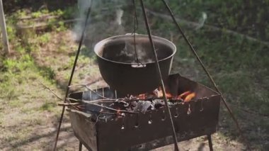 Yemek bir kazanda hazırlanır. Bovlingci kazıkta kaynıyor, arka planda ise bir çiçek tarlası var..