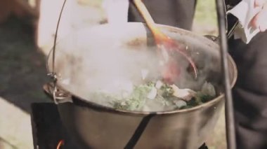 Pirinç ve sebzeli et kazıkta bir kazanda pişirilir. Aşçı malzemeleri çırpıcıyla karıştırır. Pilav hazırlama.