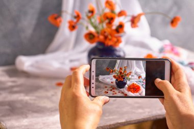 El telefonu tutar ve fotoğraf çeker gelinciklerin natürmortlarının