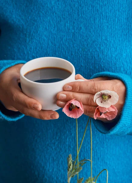 Girl holding poppy flowers and a White cup of warm morning coffee. Blue background.