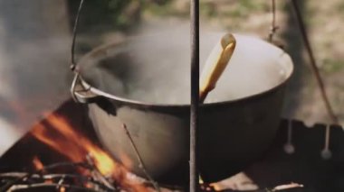 Yemek bir kazanda hazırlanır. Bovlingci kazıkta kaynıyor, arka planda ise bir çiçek tarlası var..
