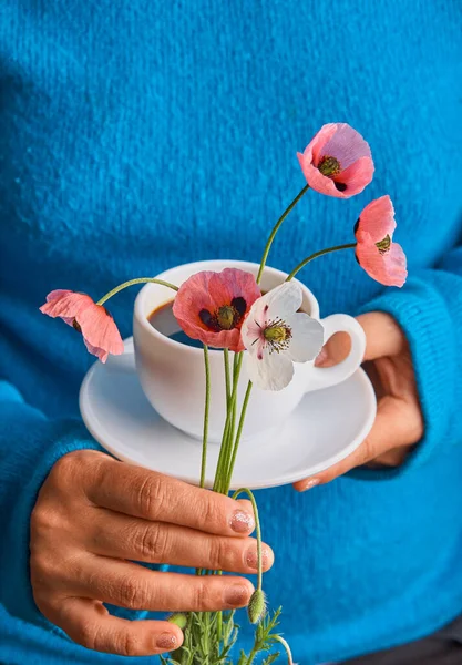 Girl holding poppy flowers and a White cup of warm morning coffee. Blue background.