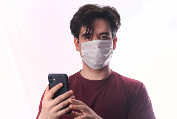 Ένας Νεαρός Ιατρική Μάσκα Χρησιμοποιεί Ένα Τηλέφωνο Απομονωμένο Λευκό Φόντο — Φωτογραφία Αρχείου