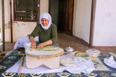 An elderly Turkish woman makes a traditional dish - a baked flat pancake Gozleme clipart