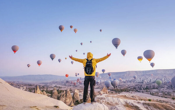 На рассвете турист с рюкзаком на фоне парящих воздушных шаров в Каппадокии, Турция
