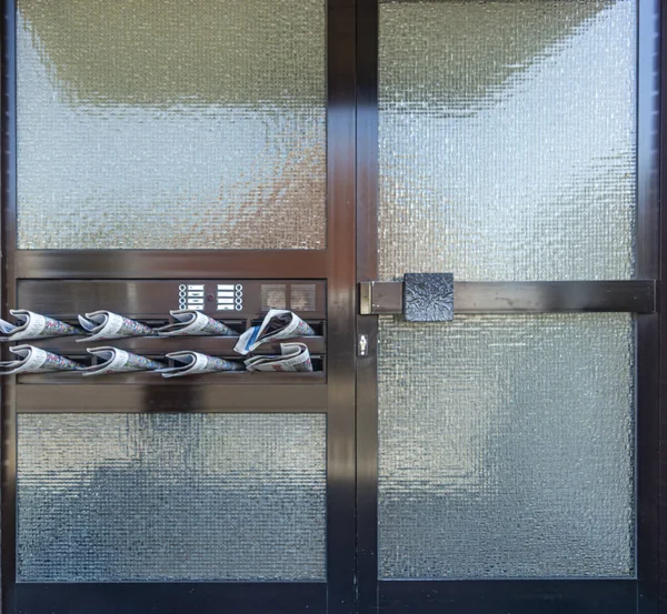 Glass door with newspapers in mailboxes closeup — Stock Photo, Image