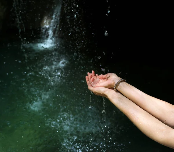 Pure mountain river water in the hands of a woman, dripping from above. Women\'s hands with water splashes