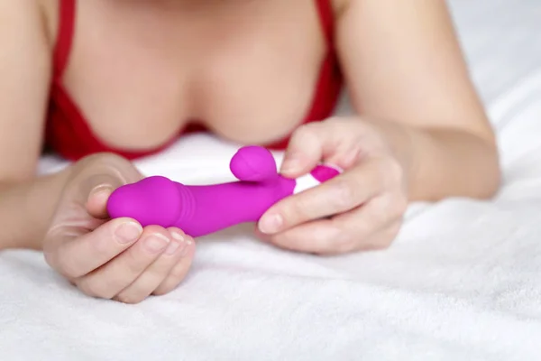 Vibratör kadınların elinde, seks oyuncakları konsepti. Yatağa uzanmış, elinde mor silikon G noktası dildosu tutan bir kadın.