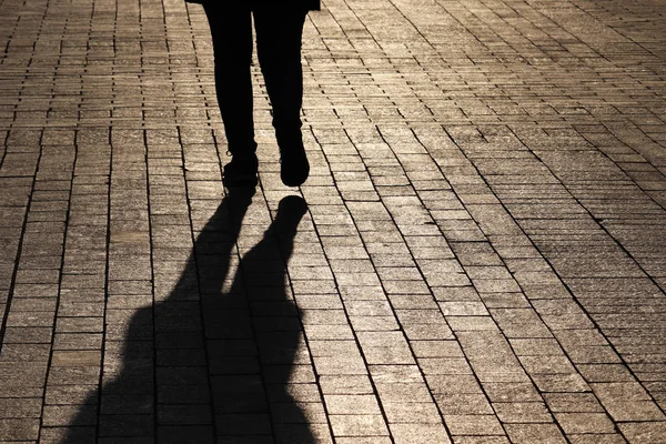 Silhouette and shadow of woman walking down on a street, rear view. Concept of loneliness, parting, dramatic stories, human life