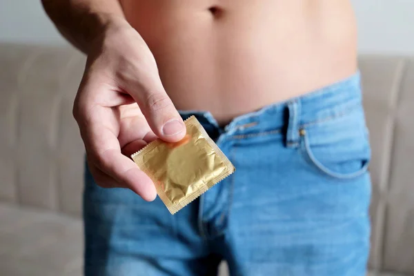 Condom in male hand close up, safe sex. Man in jeans with naked torso, concept of contraception, AIDS prevention