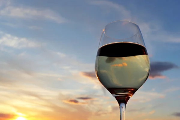Glass of white wine on colorful sunset background, sun and sky are reflected in alcohol drink. Concept of celebration, evening party at resort, romantic dinner outdoors