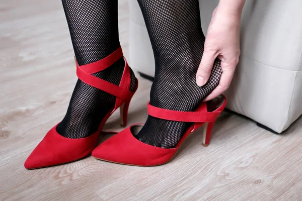 疲れた足 足の痛み 女性の高いかかとの上に赤い靴を脱いで 黒フィッシュネットストッキングの女の子で足首 女性の健康とファッションをマッサージ — ストック写真