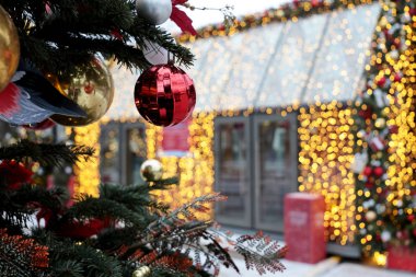 Şehirdeki bir kış caddesinde yeni yıl süslemeleri, festival ışıklarıyla evin yakınında yürüyen insanlar, gece aydınlatması. Oyuncak topları olan Noel ağacı, tatil büyüsü