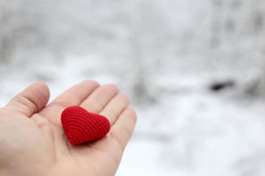 Kar ormanına karşı bir erkeğin elinde kırmızı örülmüş kalp. Romantik aşk kavramı, Sevgililer Günü, kış havası veya hayırseverlik.