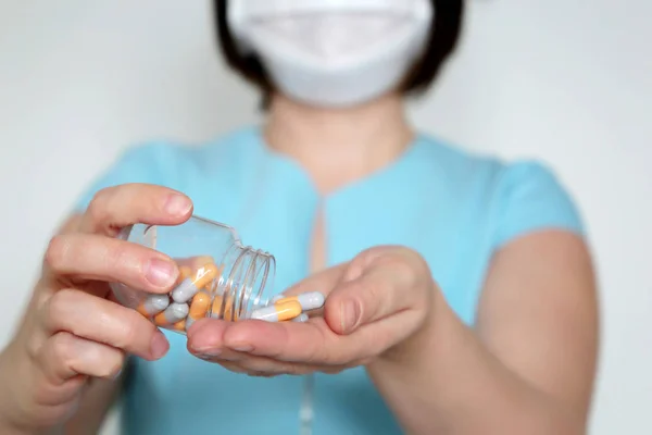 Hapları olan bir kadın, bir şişe kapsülü olan tıbbi maskeli bir doktor. İlaç, vitamin, koronavirüs ve grip tedavisi