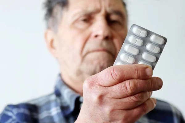 Elderly man with white pills in blister packs. Concept of medical prescription, cold treatment, Alzheimer disease