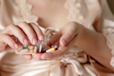 Hap alan bir kadın, kadın ellerinde bir şişe kapsül. Yatakta oturan inci sabahlıklı seksi kız, uyku ya da zayıflama hapları, mide ilacı, doğum kontrol hapları.