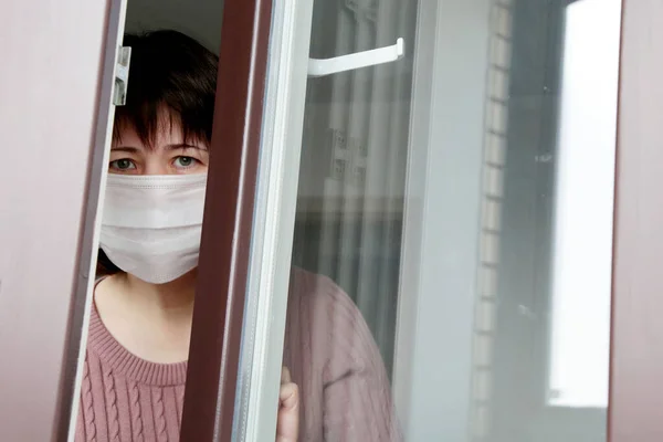 Tıbbi maskeli bir kadın pencereden dışarı bakıyor. COVID-19 koronavirüs salgını sırasında karantina