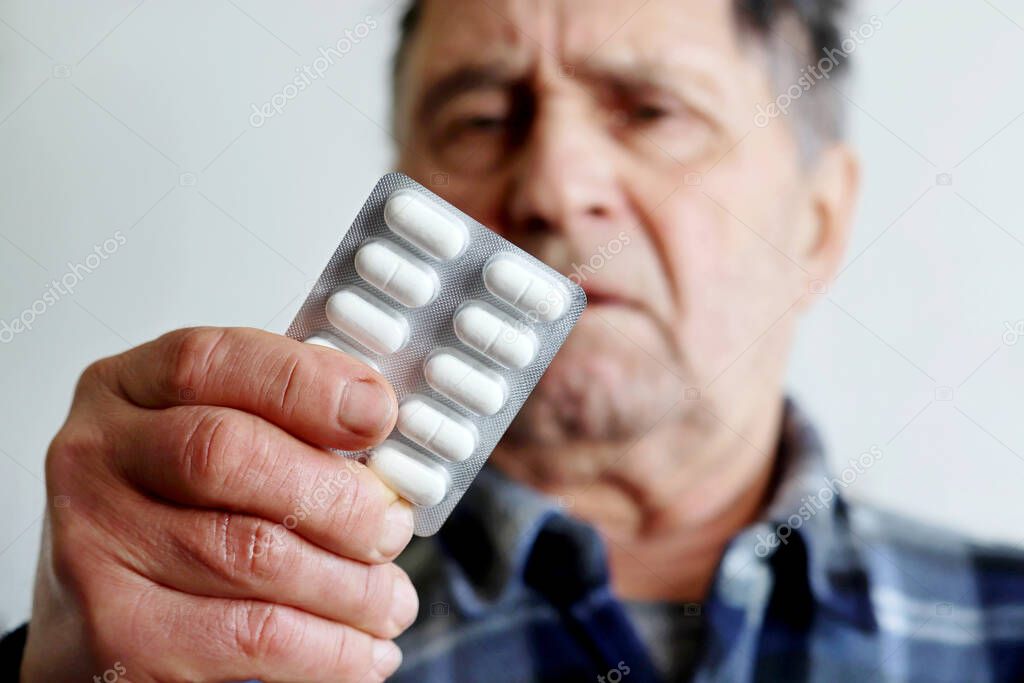 Coronavirus treatment and prevention, elderly man with white pills in blister packs. Concept of medical prescription, cold and flu, Alzheimer disease