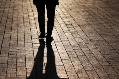 Sokakta yürüyen yalnız bir kadının silueti ve gölgesi. Kaldırımdaki kadın bacakları, yalnızlık kavramı, koronavirüs salgını sırasında şehirde karantina.