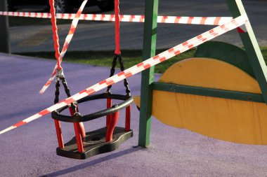 Çocuklar bir sinyal bandıyla çitle sallanıyor. Boş çocuk parkı, covid-19 koronavirüs salgını sırasında şehirde karantina.