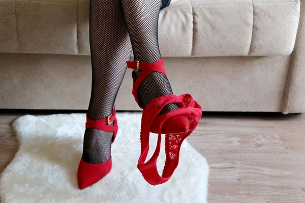 赤いパンティーを脱いだ女性の足 女性で黒フィッシュネットストッキングと靴に座ってソファ セクシーレースランジェリー — ストック写真