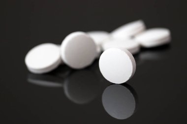 Beyaz haplar siyah arka plandaki siyah camlara, haplara yansıyor. Eczane, ilaç veya vitamin kavramı