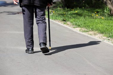 Şehir caddesinde bastonla yürüyen bir adam. Topallama kavramı, omurga hastalıkları.