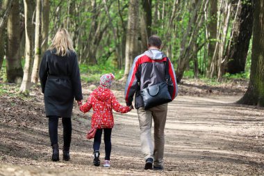 Bahar parkında el ele yürüyen çocuklu bir çift. Sarışın kadın ve küçük kızı olan bir adam, aile eğlencesi kavramı.